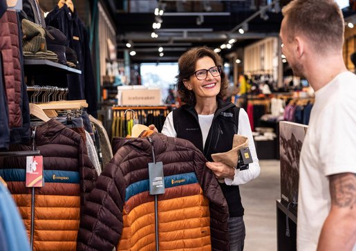 Verkaufsgespräch Daniela Baumhauer zeigt einem Kunden eine bunte Winterjacke