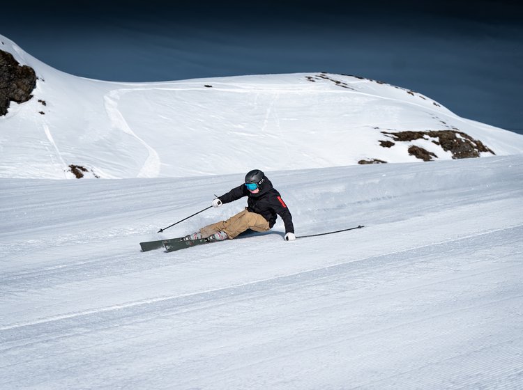 Skifahrer zieht eine sportliche Kurve auf einer präparierten Piste in verschneiter Berglandschaft.