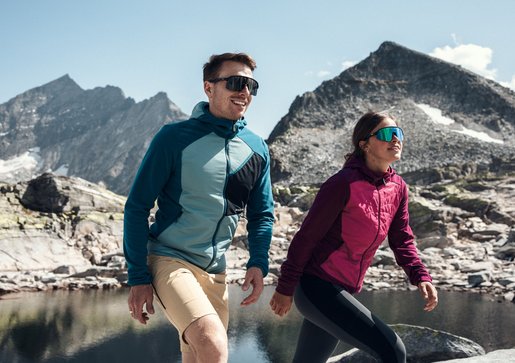 Mann und Frau in funktionaler Outdoorbekleidung wandern gemeinsam durch eine alpine Berglandschaft.